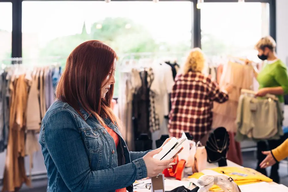 young woman looking at a handbag from the shelf to buy it, in a fashion shop. shopping concept.